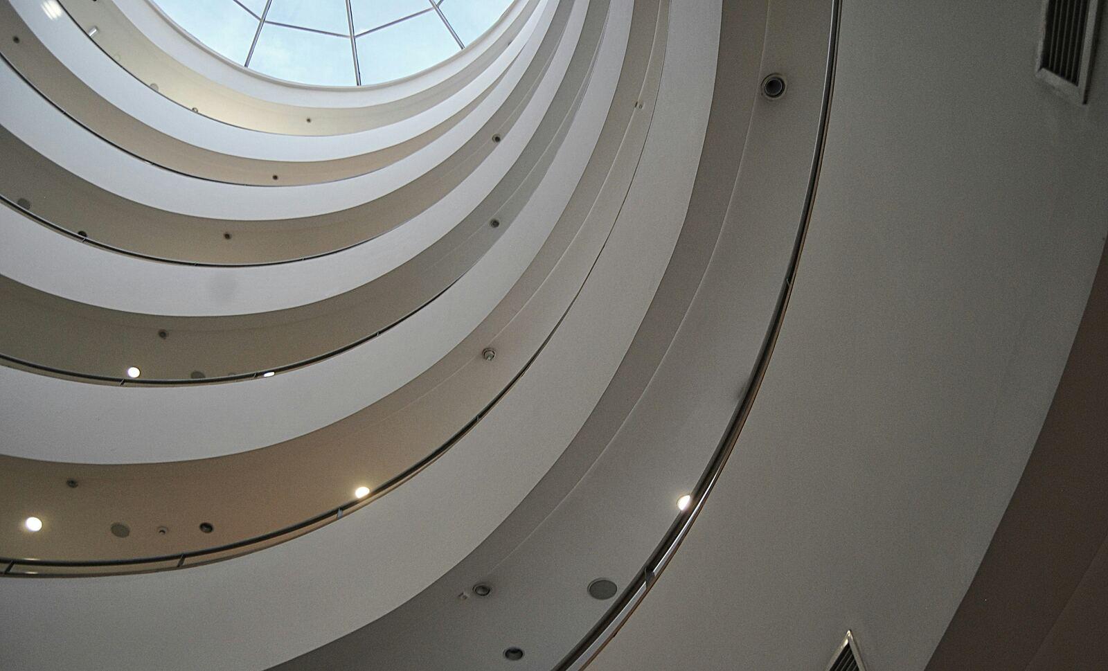 Looking up through the curved balconies of a white spiral atrium to a glass dome