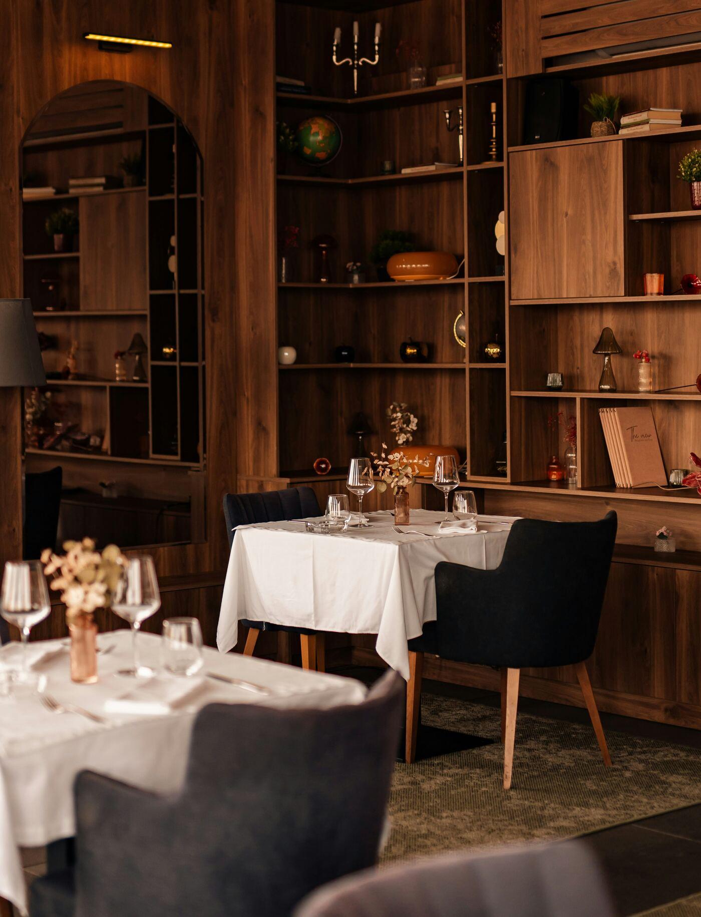 Restaurant tables laid with white linen and glassware in front of walnut shelving